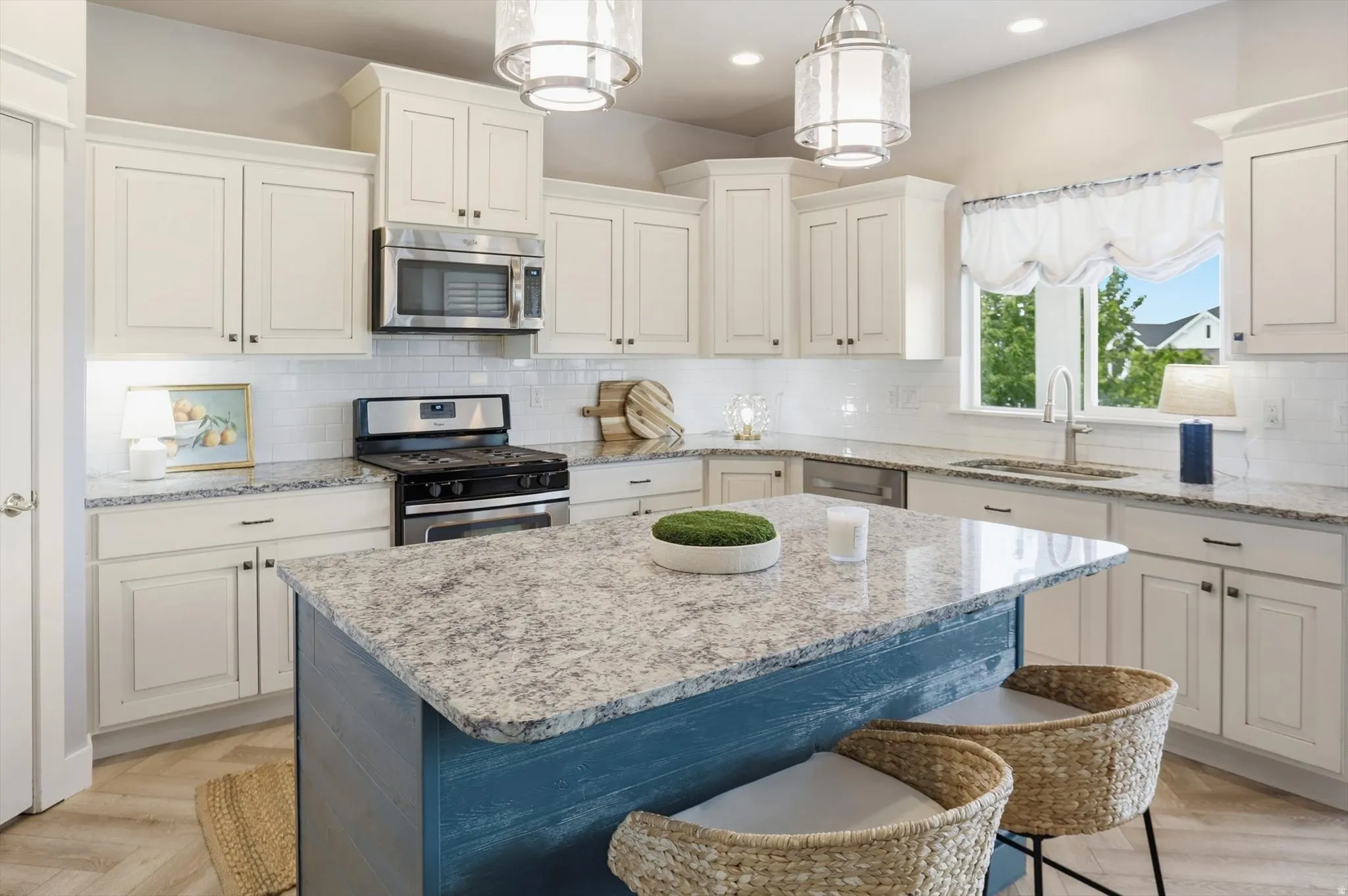 Kitchen featuring a blue-toned island with a light-toned countertop, white cabinetry with dark hardware, stainless steel appliances, and a subway tile backsplash