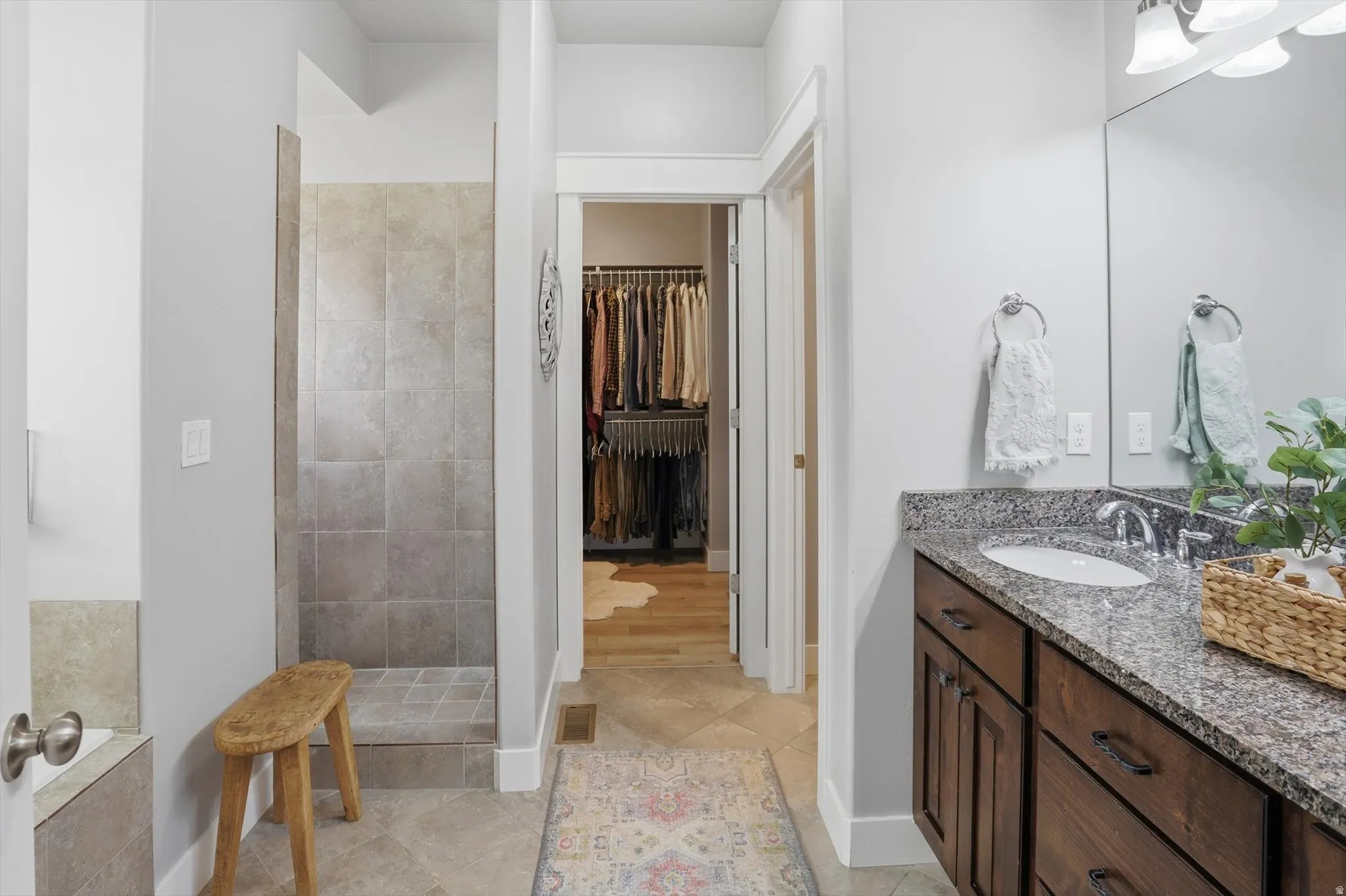 Master Bathroom featuring a walk-in shower with neutral tiling, a vanity with a granite-finish countertop, a single undermount sink, and wood-finish cabinetry