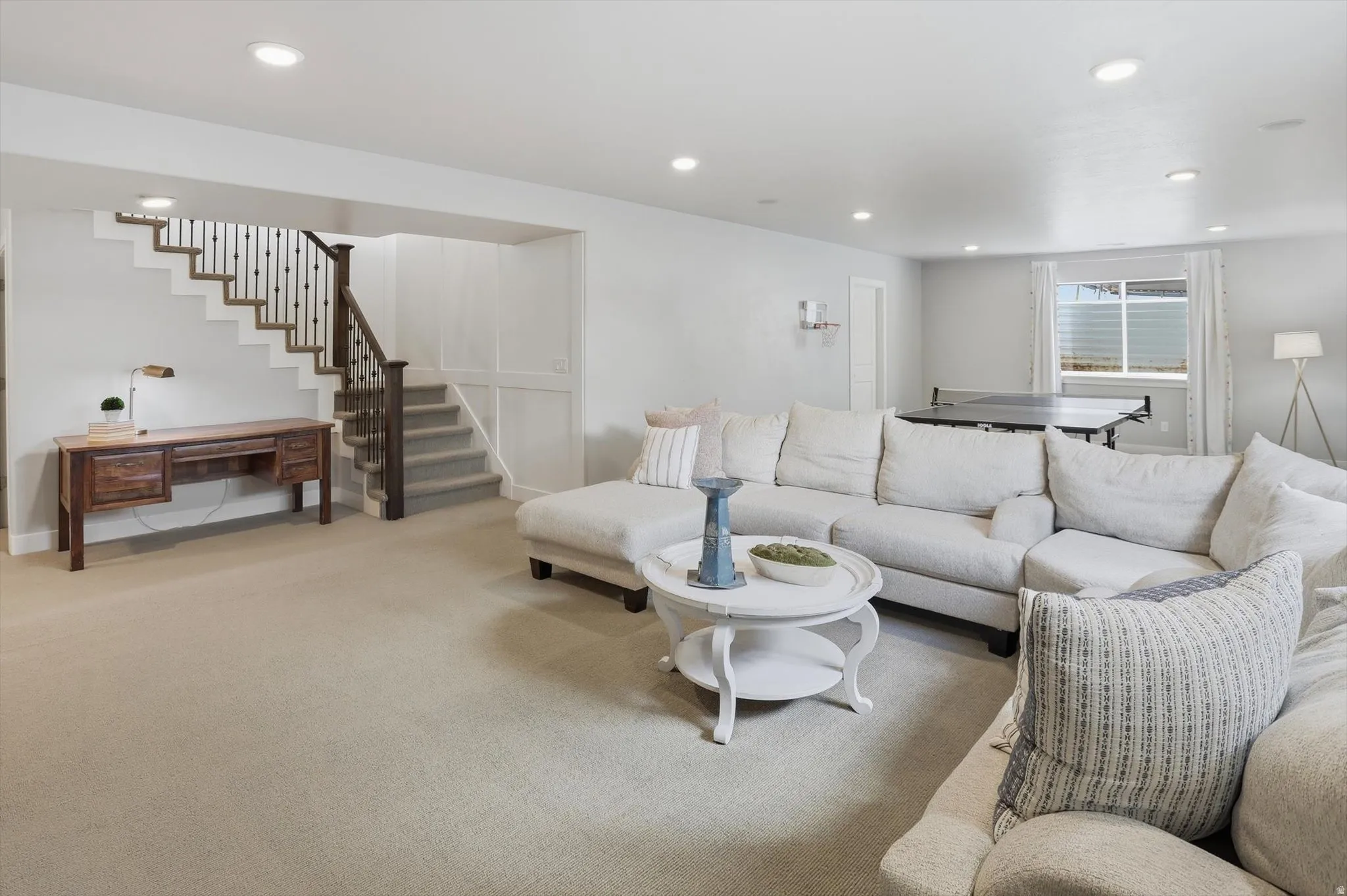 Spacious lower-level living area featuring recessed lighting, a carpeted floor, and a wooden desk with drawers