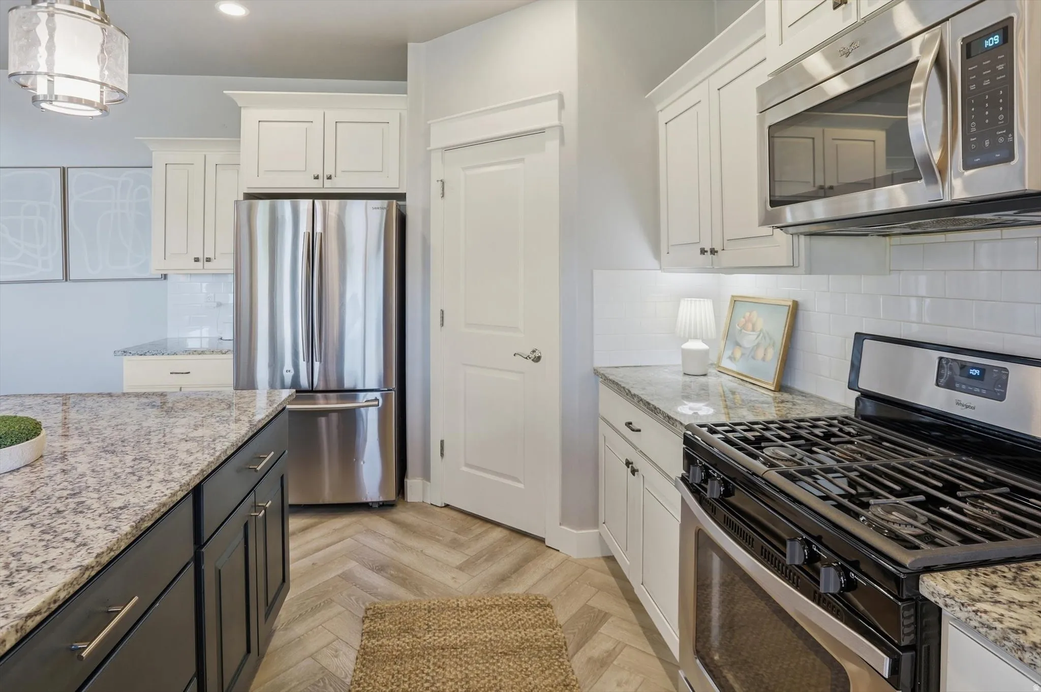 Kitchen featuring herringbone wood-finish flooring, white subway tile backsplash, granite countertops, and stainless steel appliances