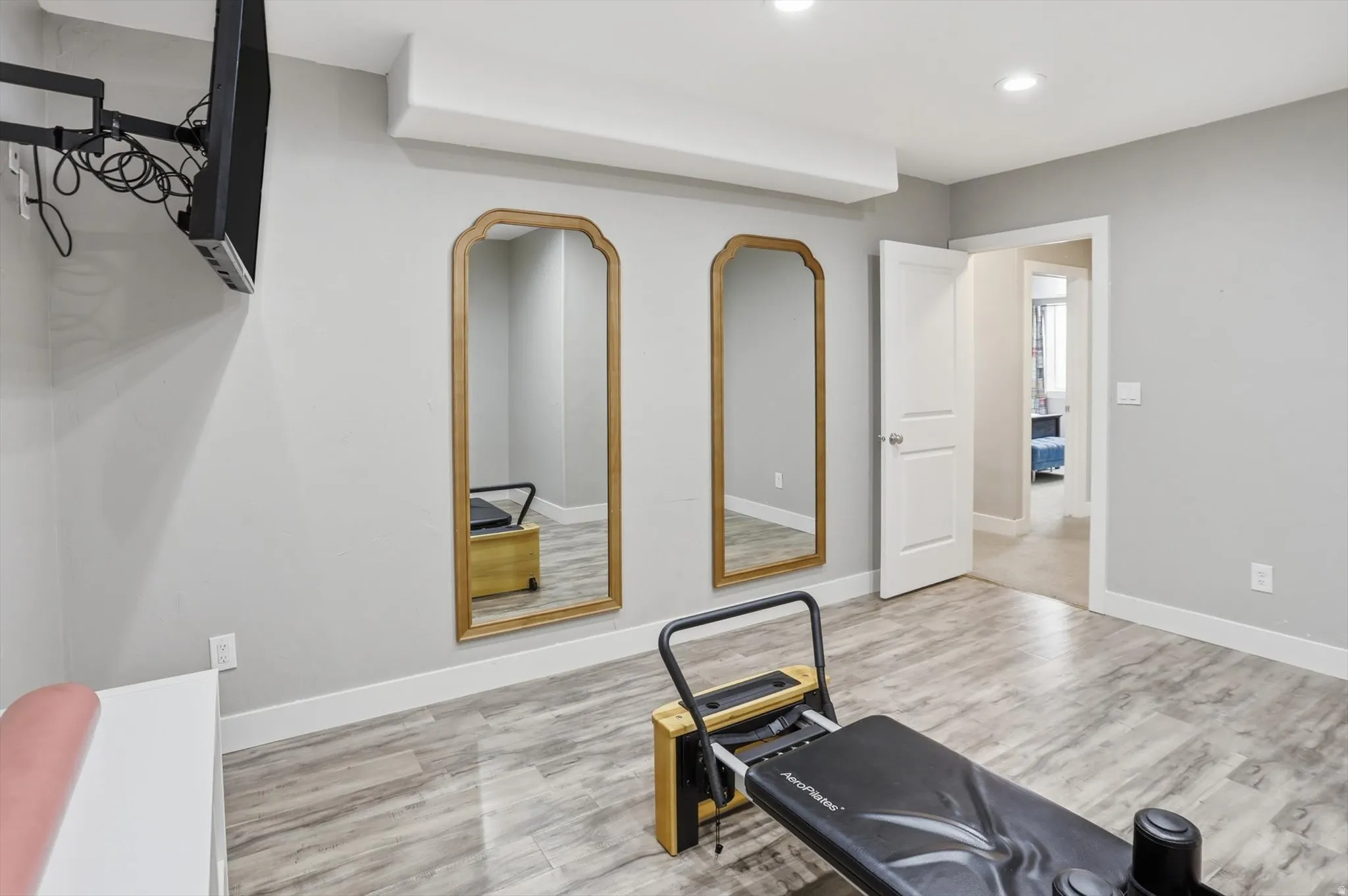 Versatile room featuring wood-finish flooring, two full-length arched mirrors, recessed ceiling lighting, and a wall-mounted display