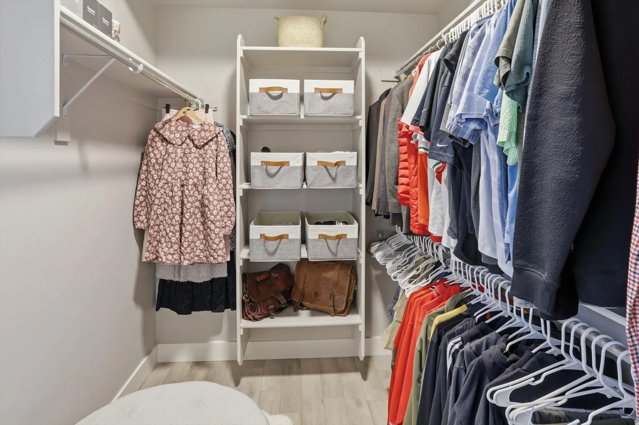 Master Walk-in closet featuring light wood-finish flooring, white shelving units, and multiple clothing rods