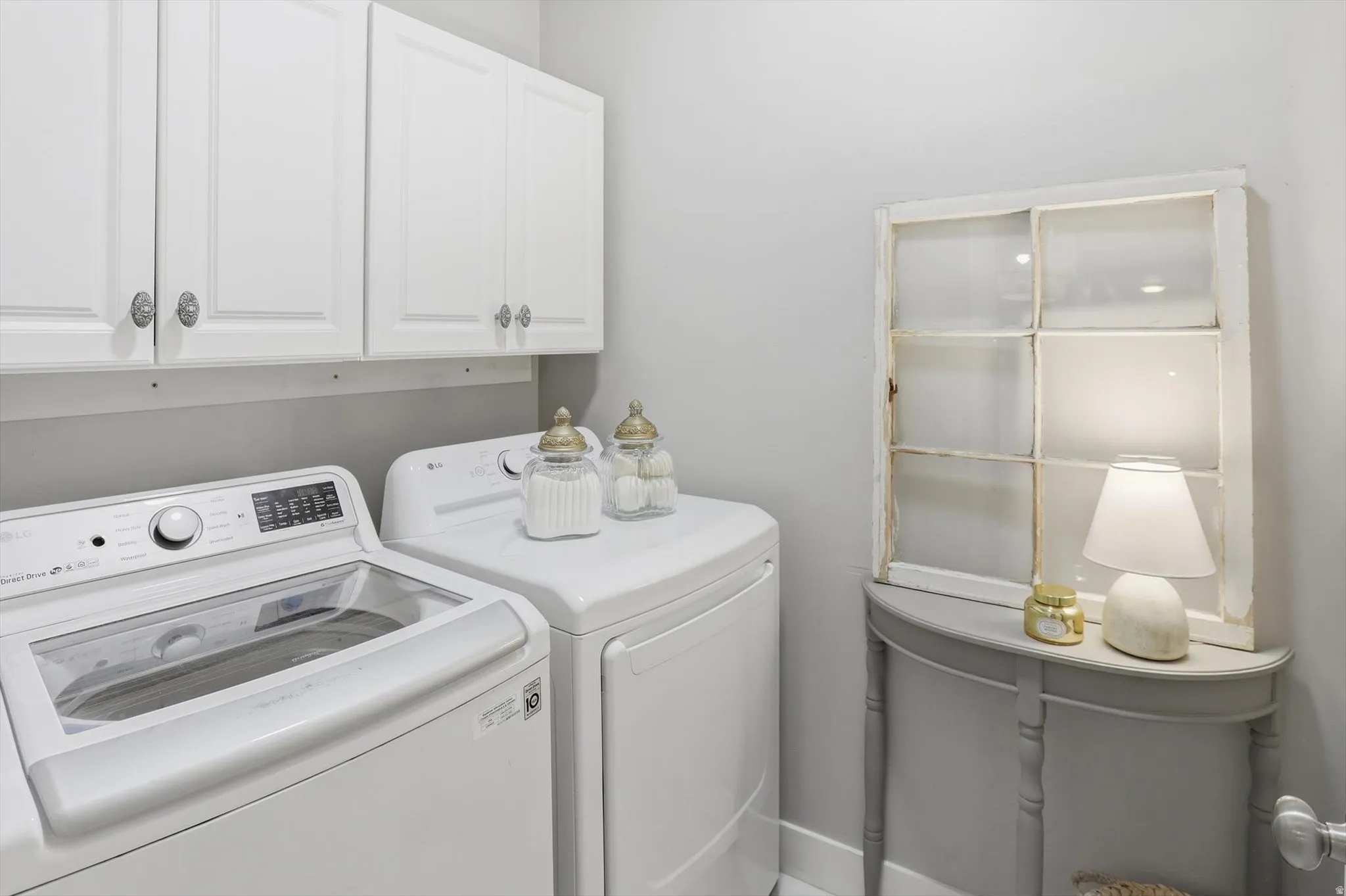 Dedicated laundry area featuring white upper cabinetry with decorative hardware, a built-in washing machine, and a built-in dryer