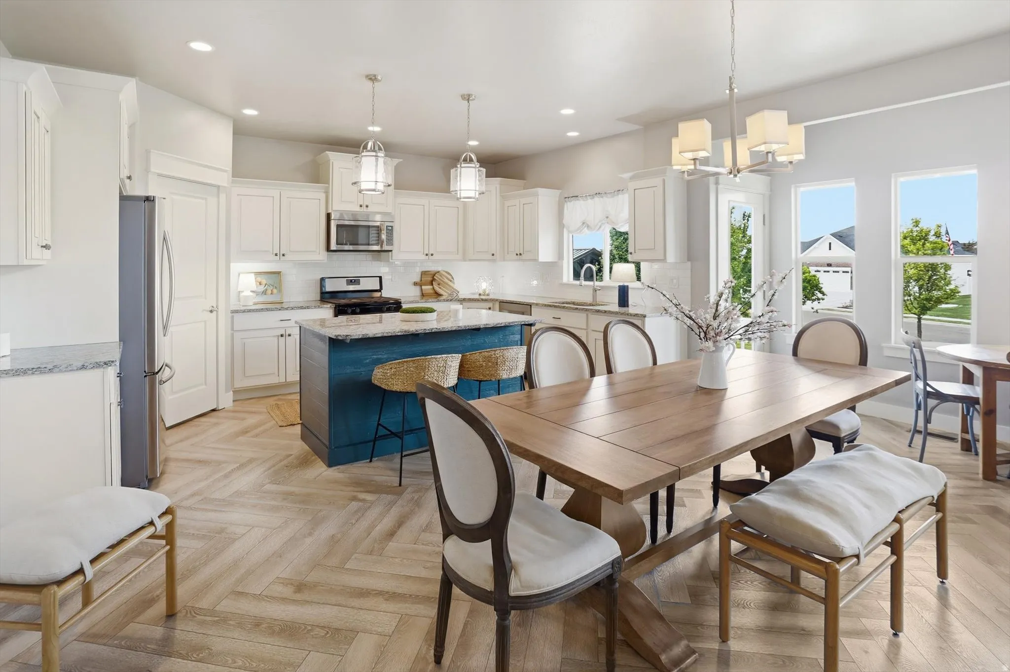 Open-concept kitchen and dining area featuring a custom blue island with counter seating, a white subway tile backsplash, and light wood-finish herringbone flooring