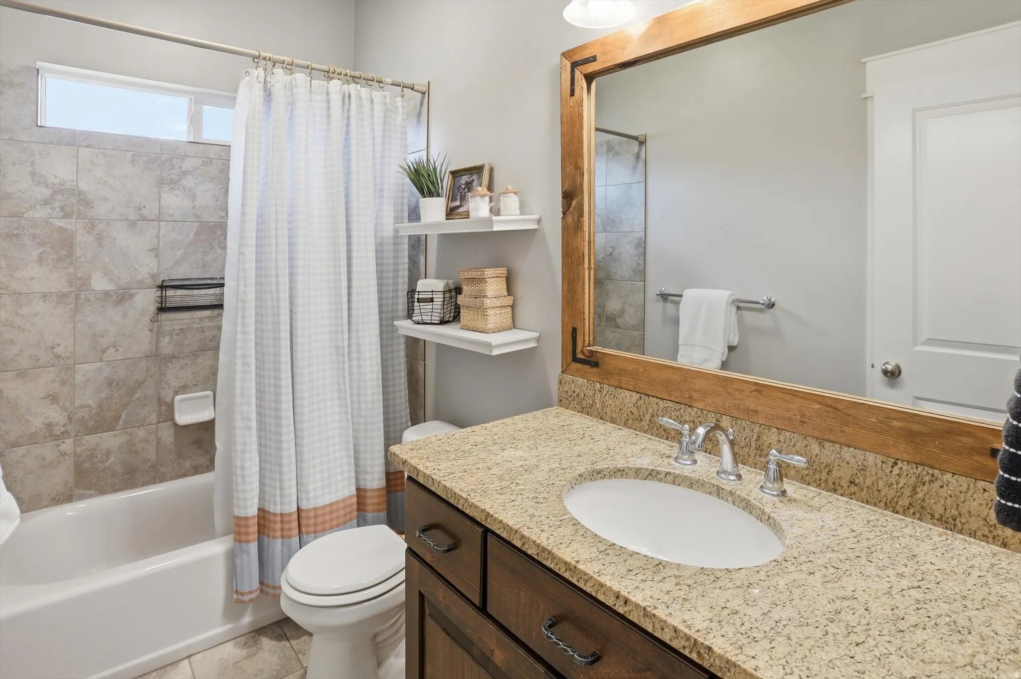 Main Bathroom featuring a wood-framed mirror, granite countertop with integrated sink, dark wood-finish vanity cabinetry, and a shower/tub combination with tiled surround and an upper transom window
