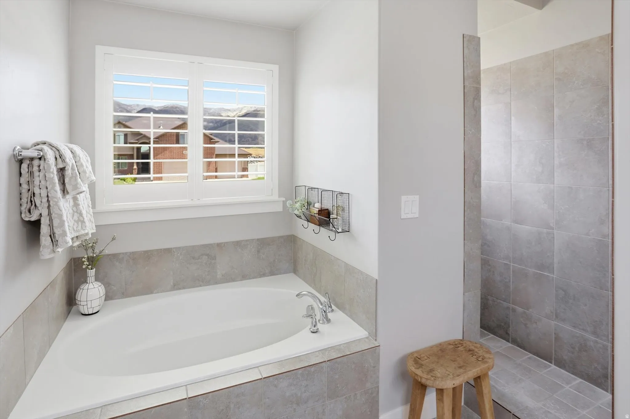 Soaking tub with tile surround, plantation shutters, and a tiled walk-in shower