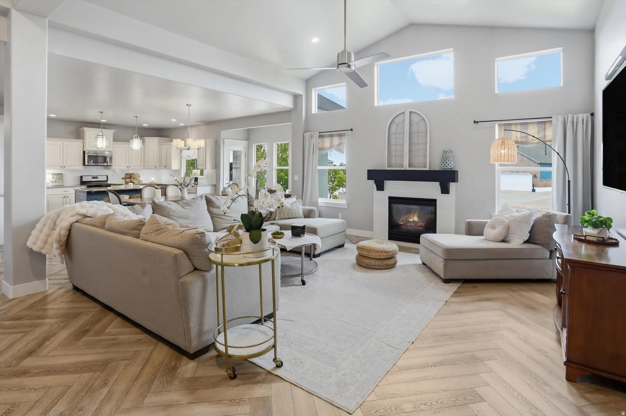 Spacious living area featuring a vaulted ceiling with a fan, a fireplace with a dark mantel, wood-finish flooring in a herringbone pattern, and transom windows