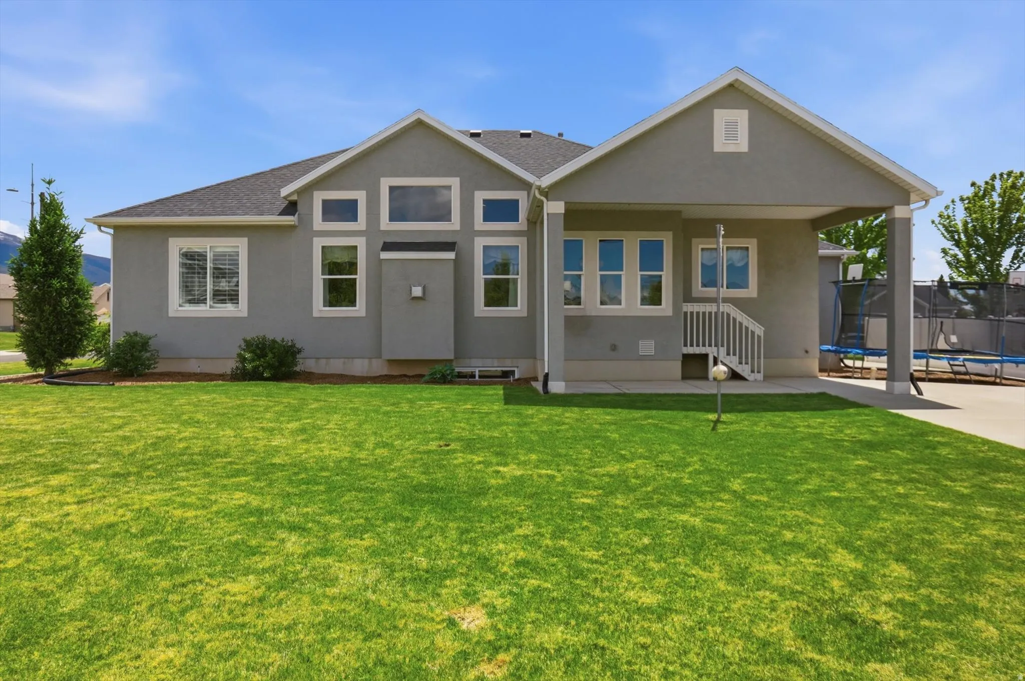 Spacious backyard featuring a manicured lawn, covered patio, and concrete driveway