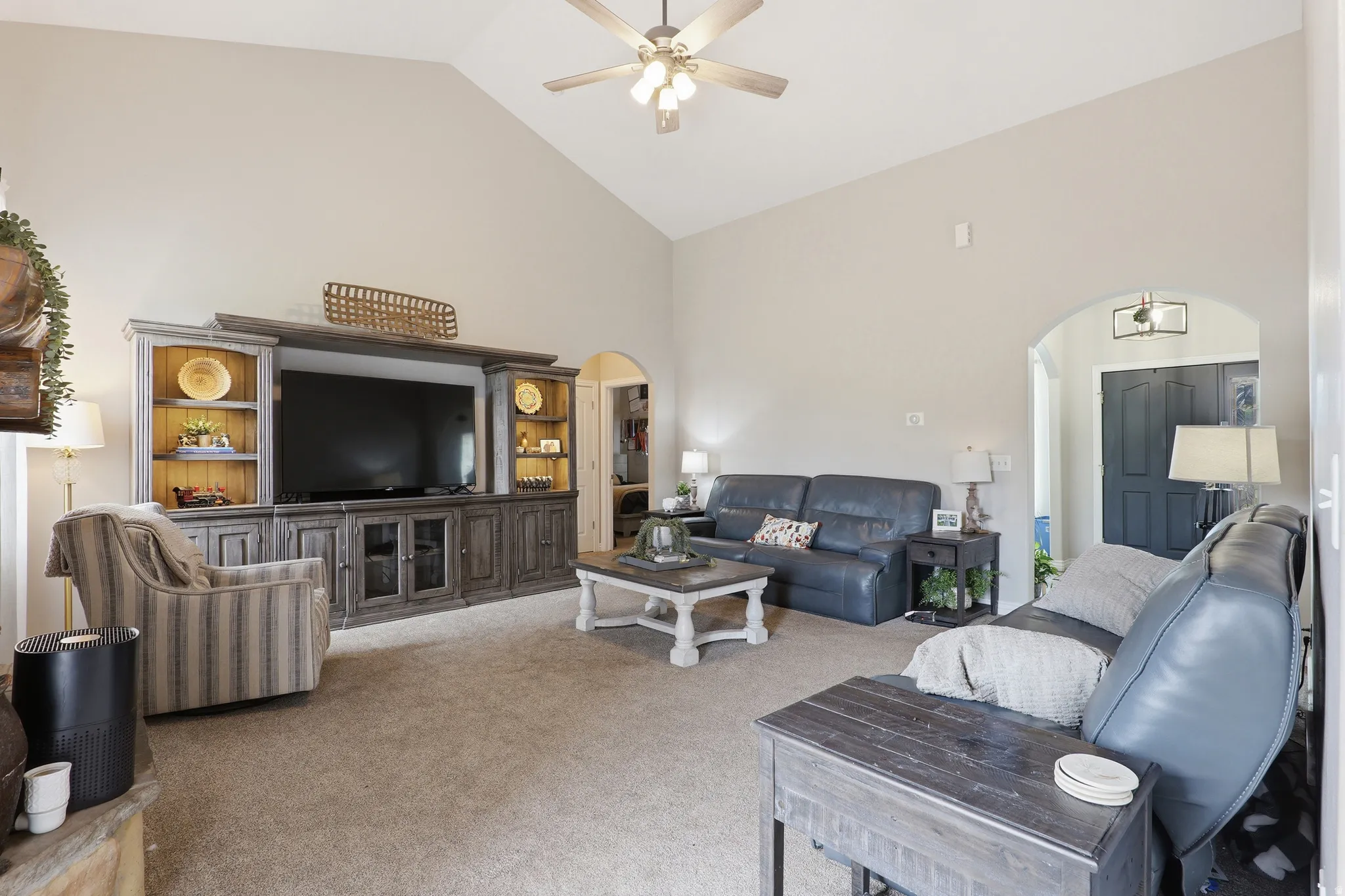 Spacious living area featuring a vaulted ceiling with a ceiling fan, carpet flooring, a built-in media console with integrated lighting, and an arched doorway