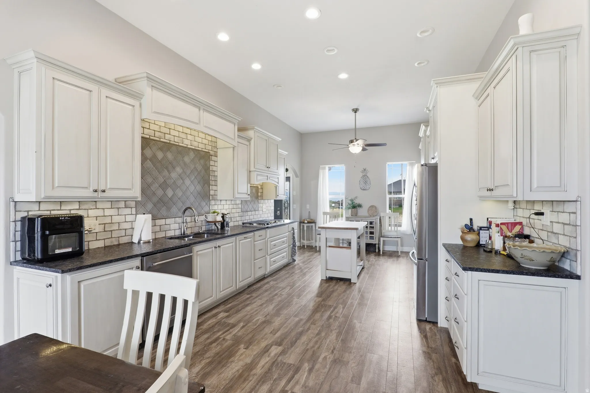 Contemporary kitchen featuring extensive white cabinetry, a dark countertop, stainless steel appliances, and wood-finish flooring