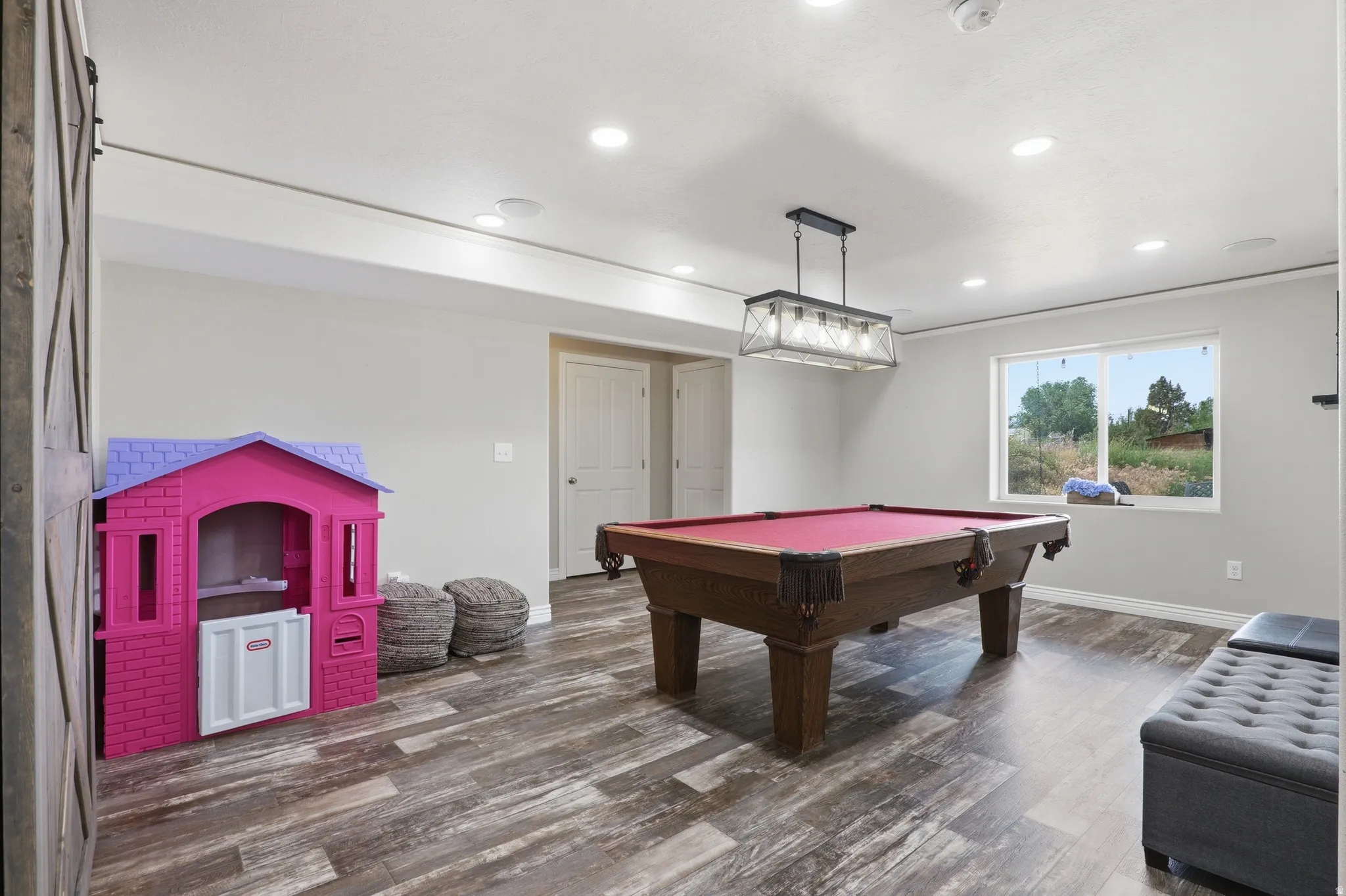 Spacious recreation room featuring wood-finish flooring, recessed lighting, and a modern industrial-style chandelier