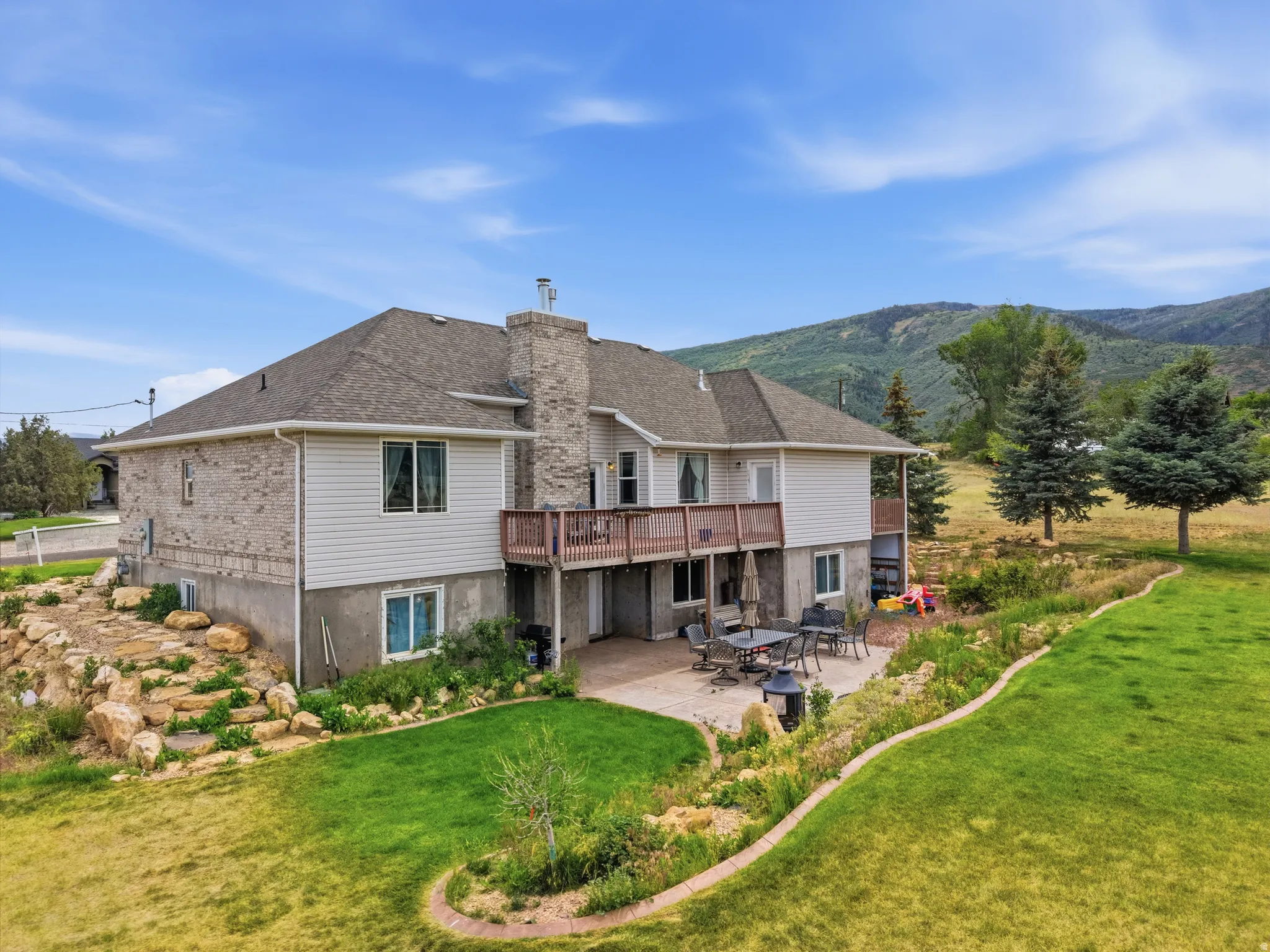 Rear exterior featuring a stone and siding facade, a second-story wood deck, and a lower-level concrete patio