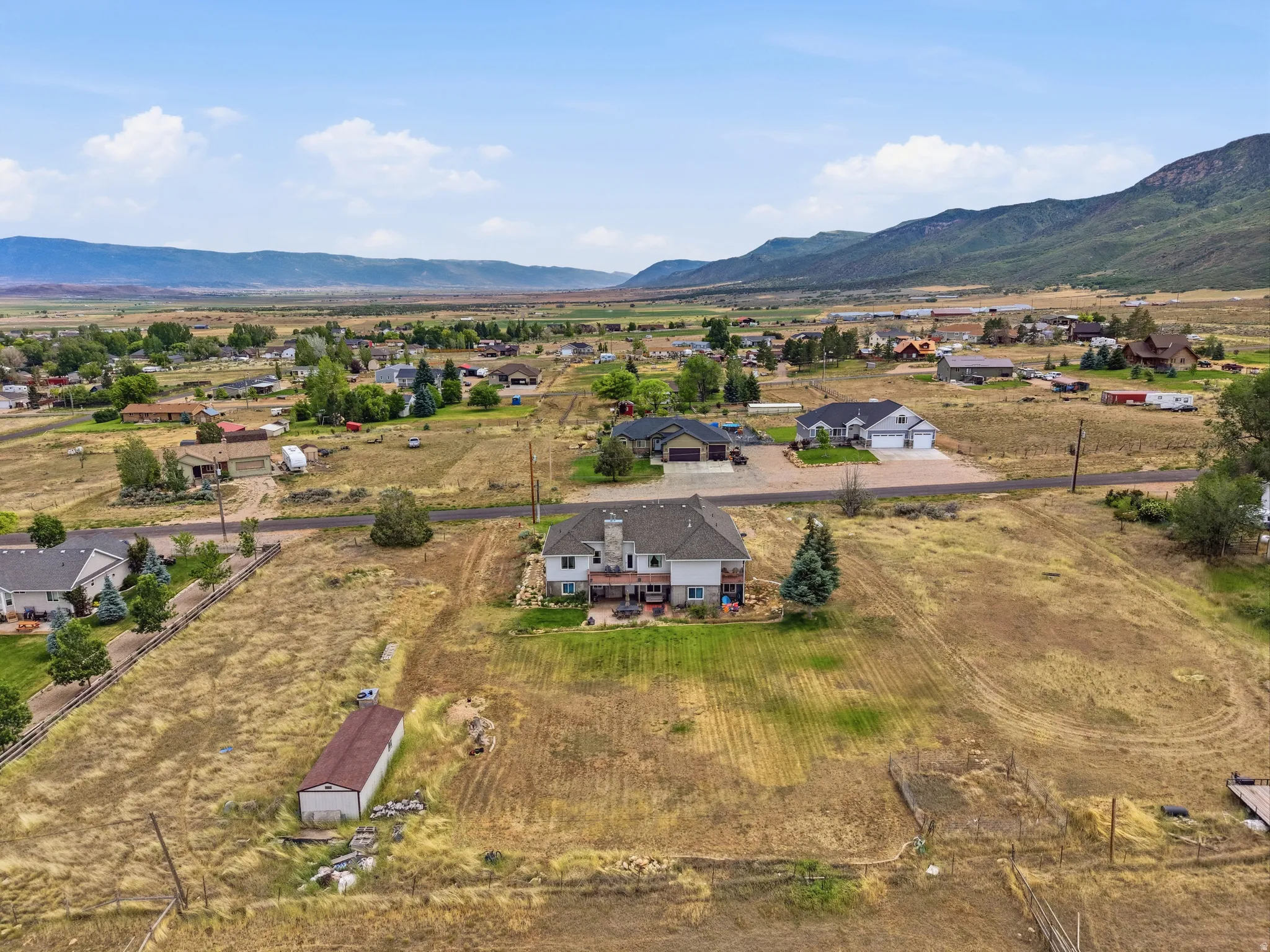 Expansive property featuring a two-story residence with a multi-level deck, a detached shed, and surrounding open land