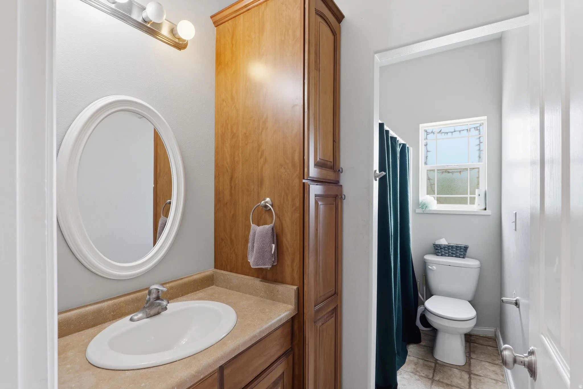 Bathroom vanity featuring a white oval mirror, three-light fixture, wood-finish cabinetry, and solid surface countertop with an integrated sink