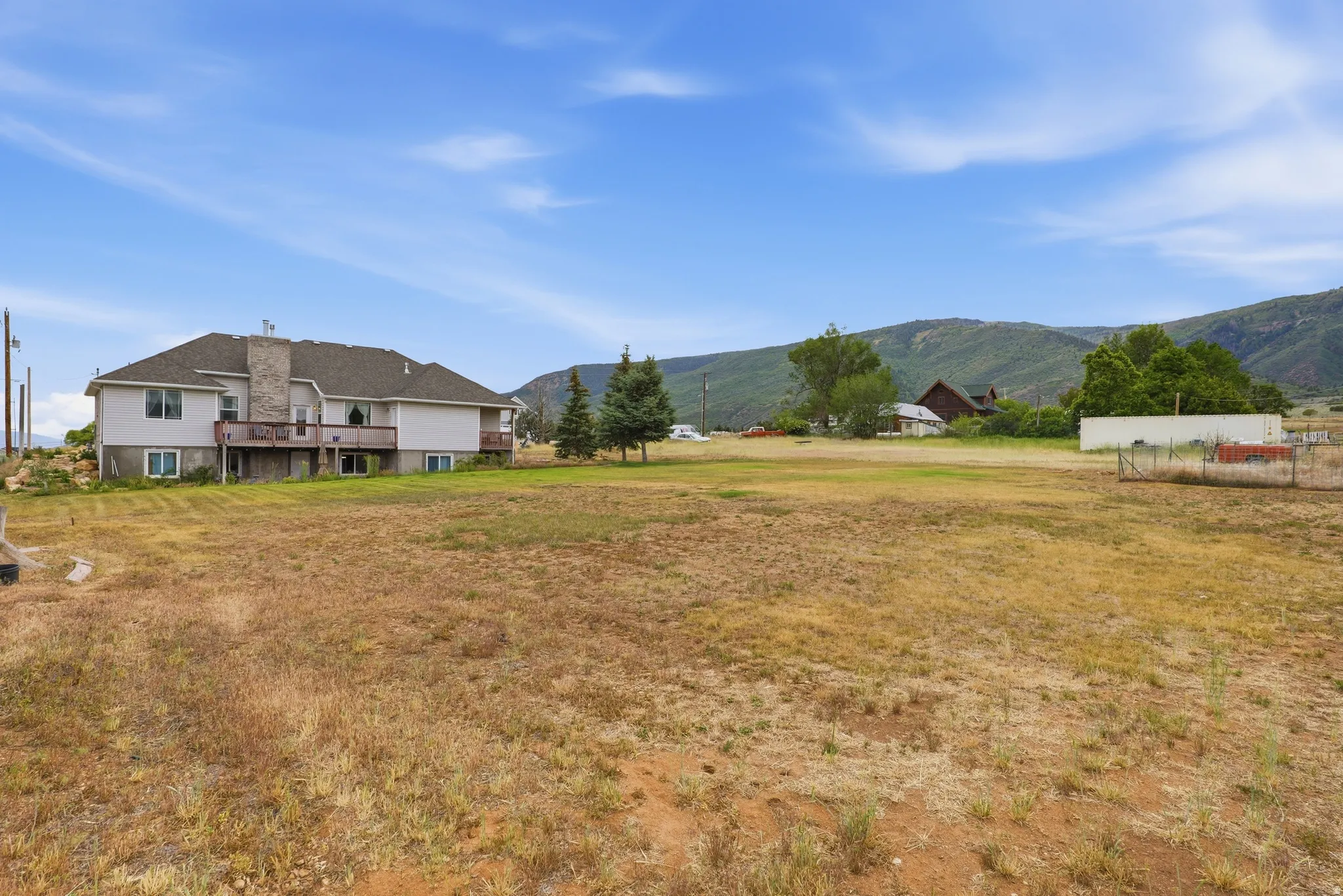 Expansive rural lot featuring a multi-level residence with light-colored siding and a stone chimney