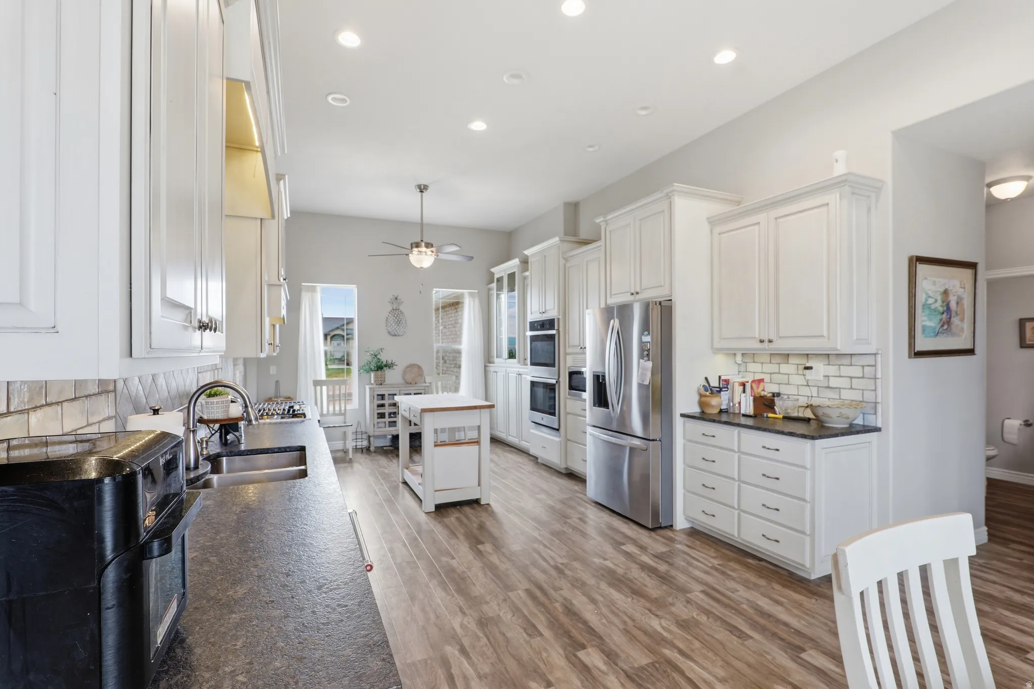 Spacious kitchen featuring extensive white cabinetry, stainless steel appliances, dark countertops, wood-finish flooring, and recessed lighting