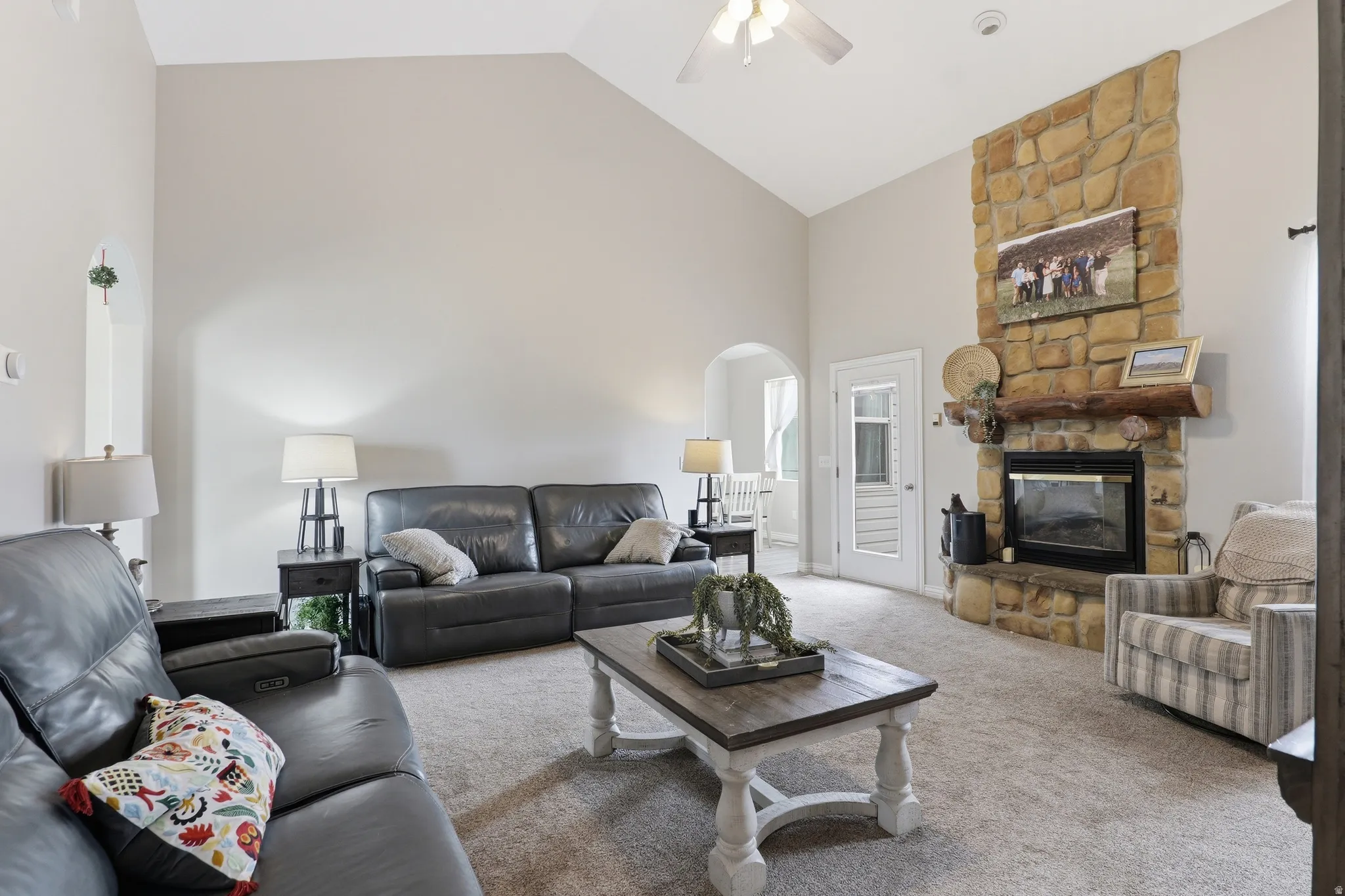 Vaulted ceiling living area featuring a floor-to-ceiling stone fireplace with a substantial log mantel