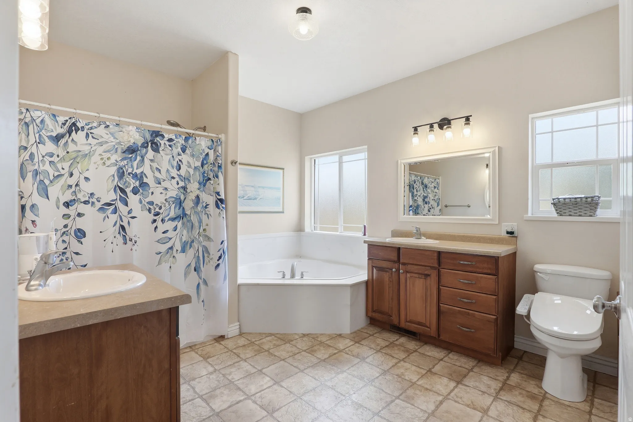 Well-appointed bathroom featuring a corner soaking tub, a single vanity with wood cabinetry and countertop, a second single vanity with wood cabinetry and countertop, a toilet, and grid-patterned flooring