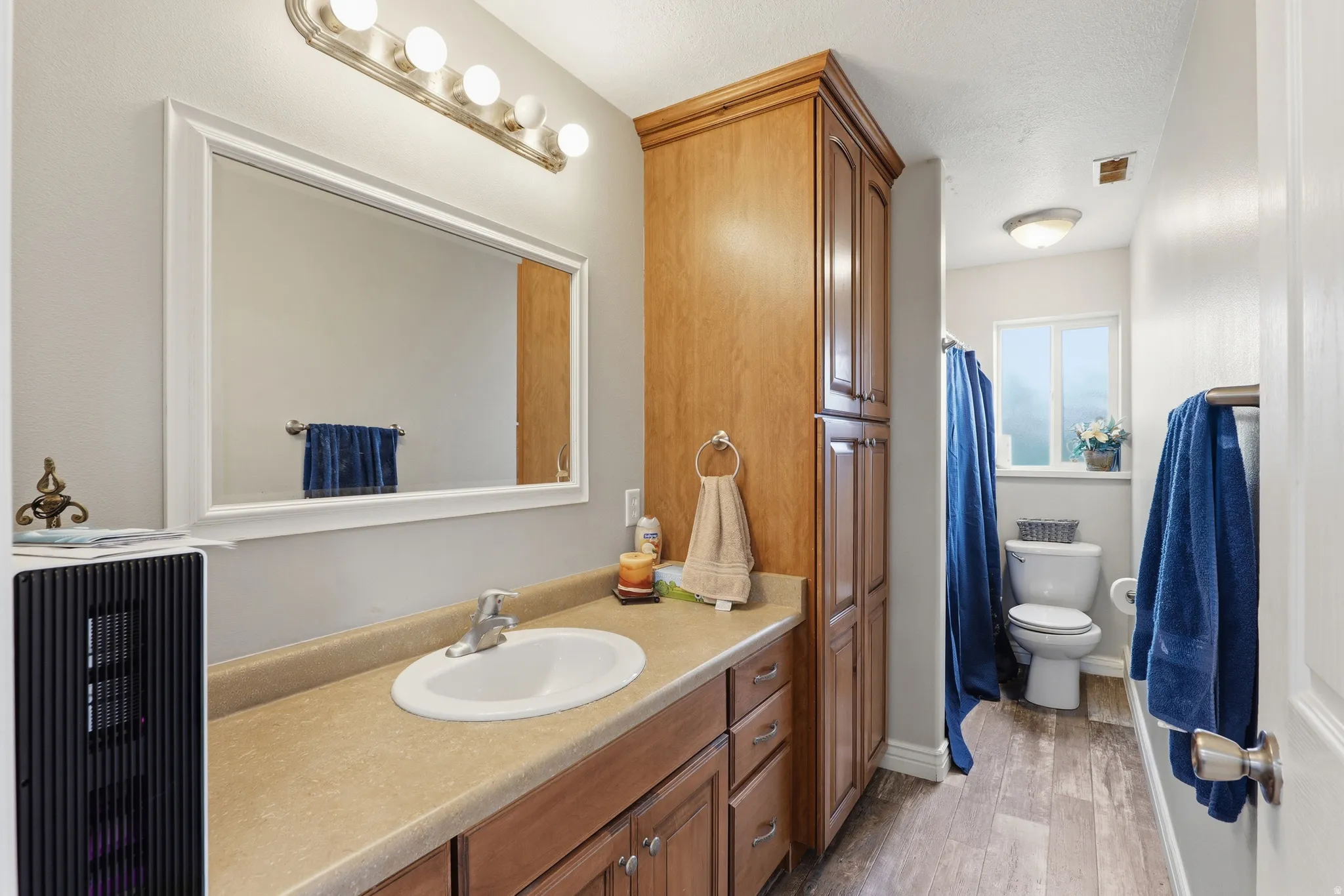Bathroom featuring a wood-finish vanity with an integrated sink and light-toned countertop, a large framed mirror, and a wood-finish linen tower