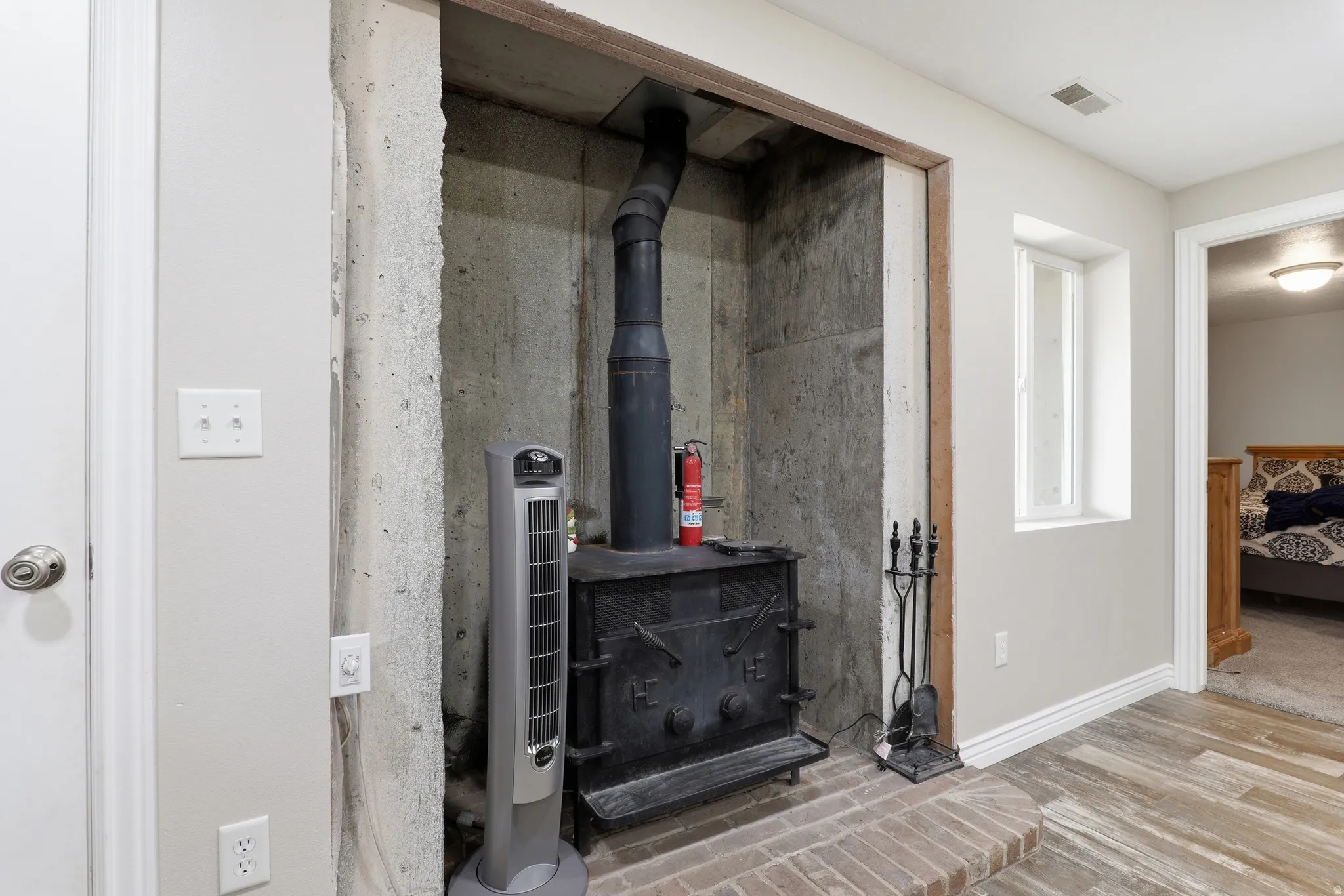 Cast iron wood-burning stove set within a concrete-lined alcove, featuring a brick hearth and a black stovepipe