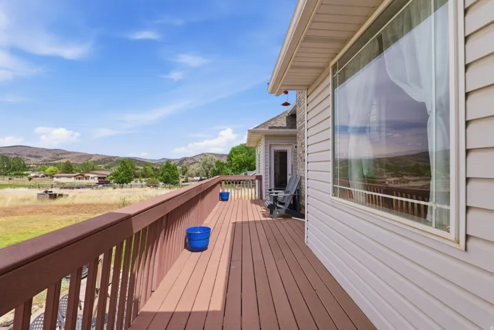 Expansive exterior deck featuring a brown wood-finish surface, matching railing, and a mountain backdrop