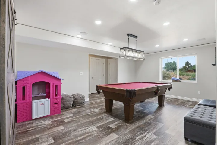 Spacious recreation room featuring wood-finish flooring, recessed lighting, and a modern industrial-style chandelier
