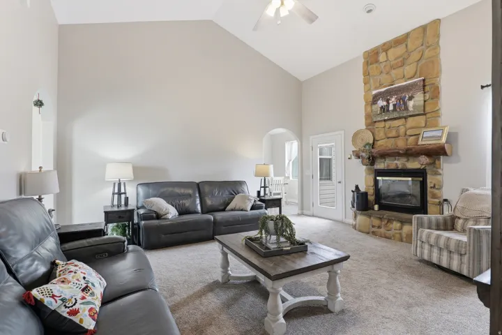 Vaulted ceiling living area featuring a floor-to-ceiling stone fireplace with a substantial log mantel