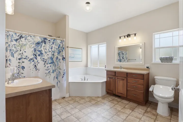 Well-appointed bathroom featuring a corner soaking tub, a single vanity with wood cabinetry and countertop, a second single vanity with wood cabinetry and countertop, a toilet, and grid-patterned flooring