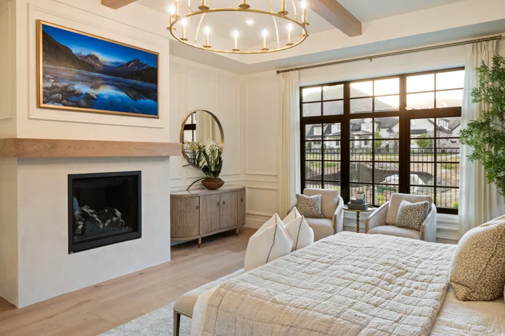 Bedroom with a decorative wall, light wood-style flooring, a fireplace, suspended lighting, and beamed ceiling