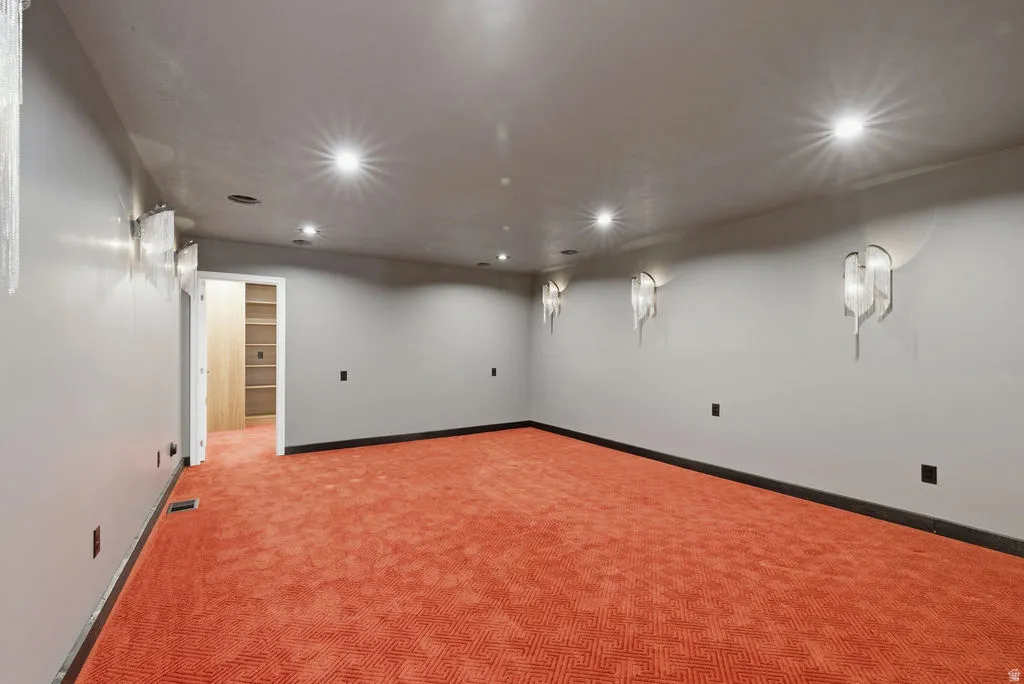 Spacious room featuring patterned orange carpeting, recessed ceiling lighting, and multiple decorative wall sconces