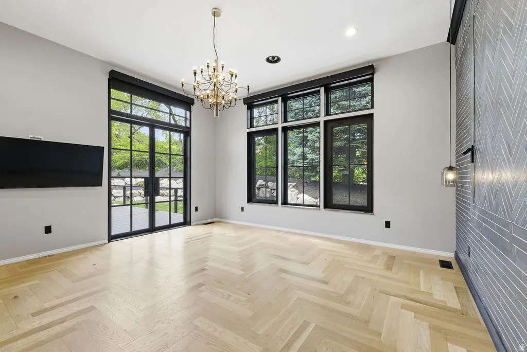 Spacious room with light wood-finish herringbone flooring, black-framed French doors, and transom windows