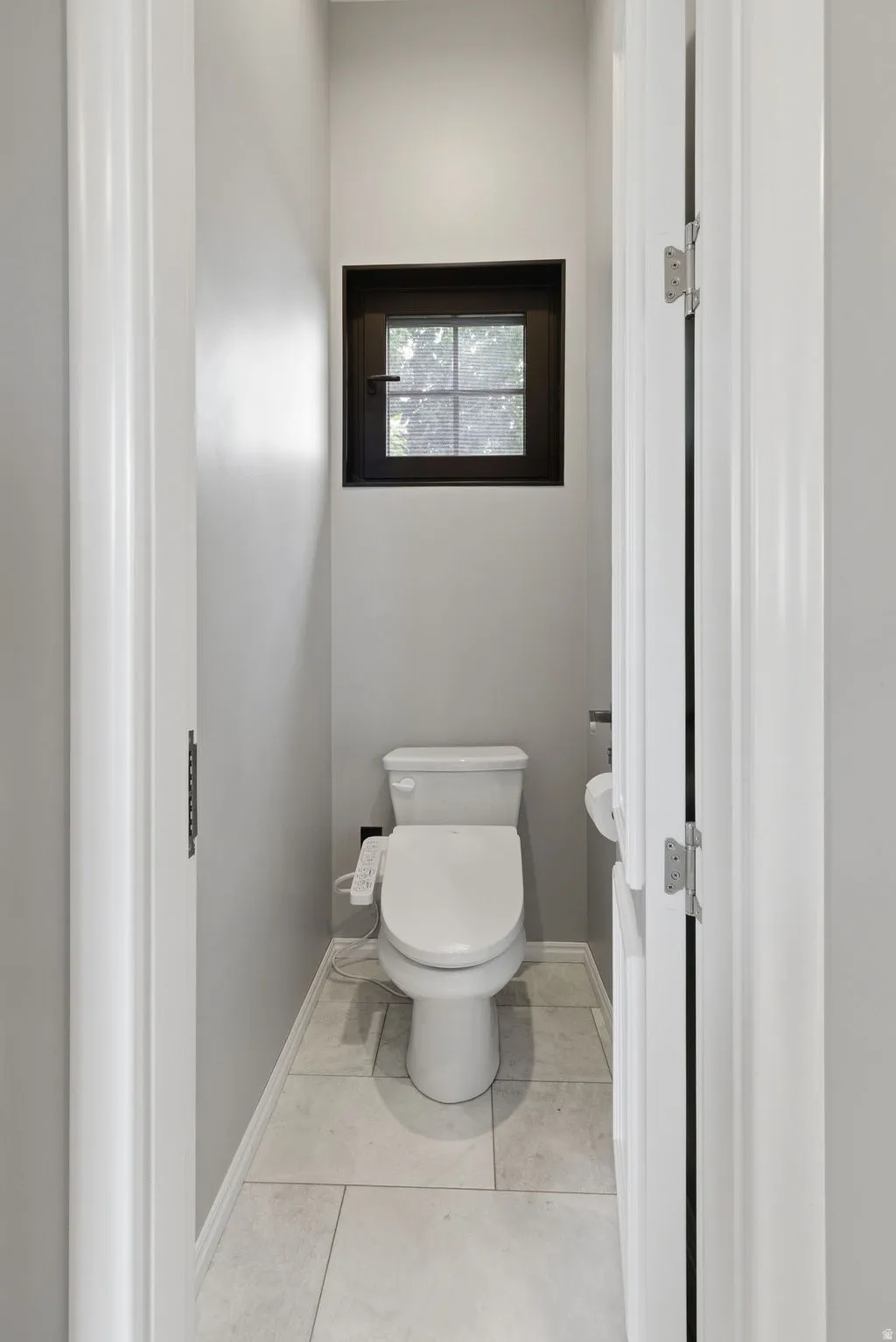 Powder room featuring a square window with dark trim, light-toned tile flooring, and a white toilet