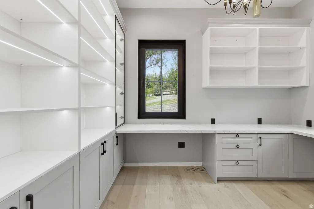 Built-in custom cabinetry with integrated lighting, a spacious L-shaped desk with a light-toned countertop, and wood-finish flooring