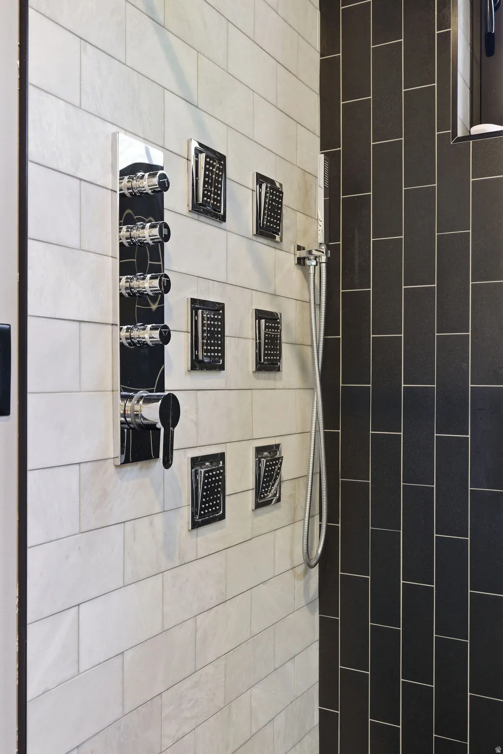 Shower featuring an integrated control panel with multiple body sprays, a handheld shower fixture, and contrasting subway tile in black and white finishes