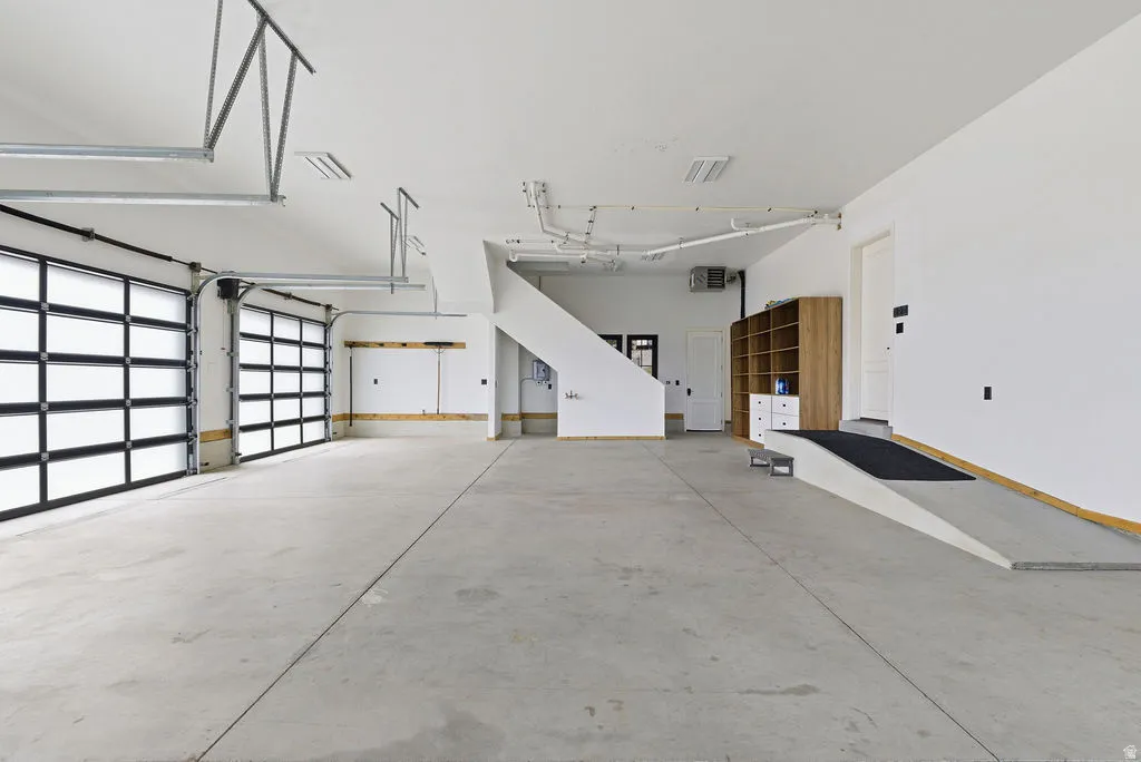 Spacious garage featuring a concrete floor, two modern glass-paneled garage doors, white painted walls, and an interior ramp