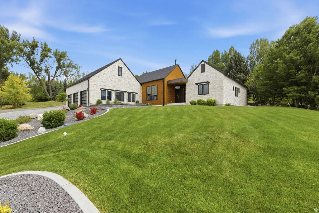 Modern farmhouse architecture featuring a white stone exterior, black-framed windows, a dark roof, and wood-paneled accents