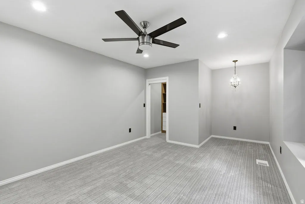 Spacious room featuring light gray carpeting and walls, a modern ceiling fan, recessed lighting, and a crystal chandelier