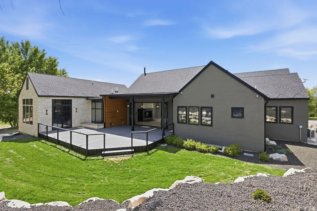 Expansive exterior featuring a large composite deck with cable railings, a covered patio area with a built-in fireplace, and a manicured lawn