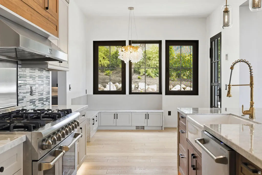Gourmet kitchen featuring a professional-grade range with a stainless steel hood, an integrated dishwasher, and light wood-finish flooring