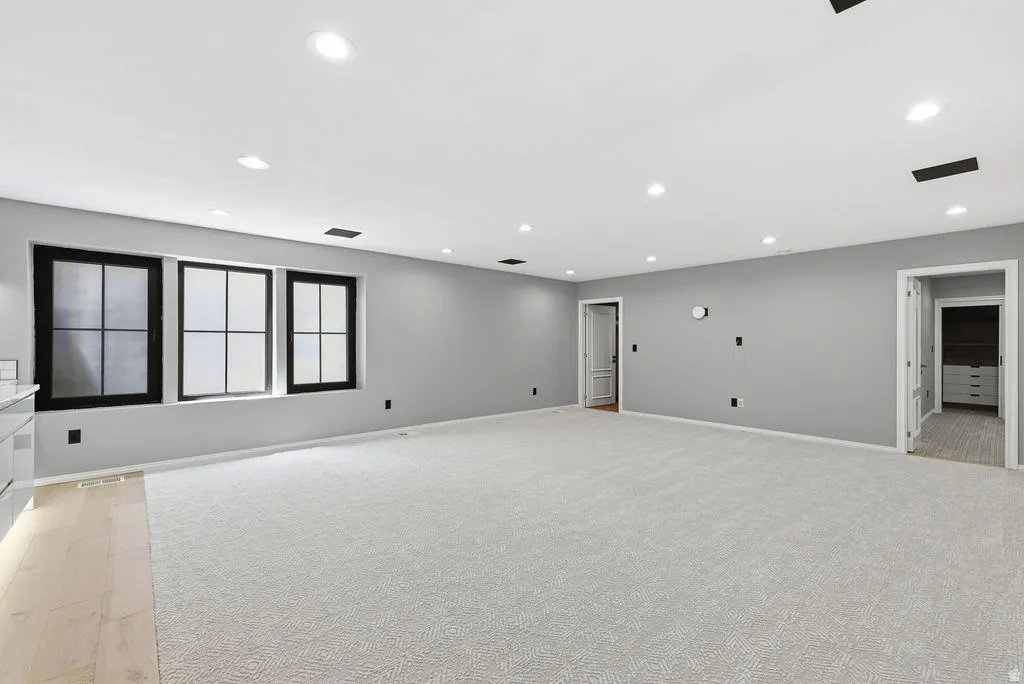 Spacious room featuring light gray carpeting, recessed lighting, and three black-framed windows