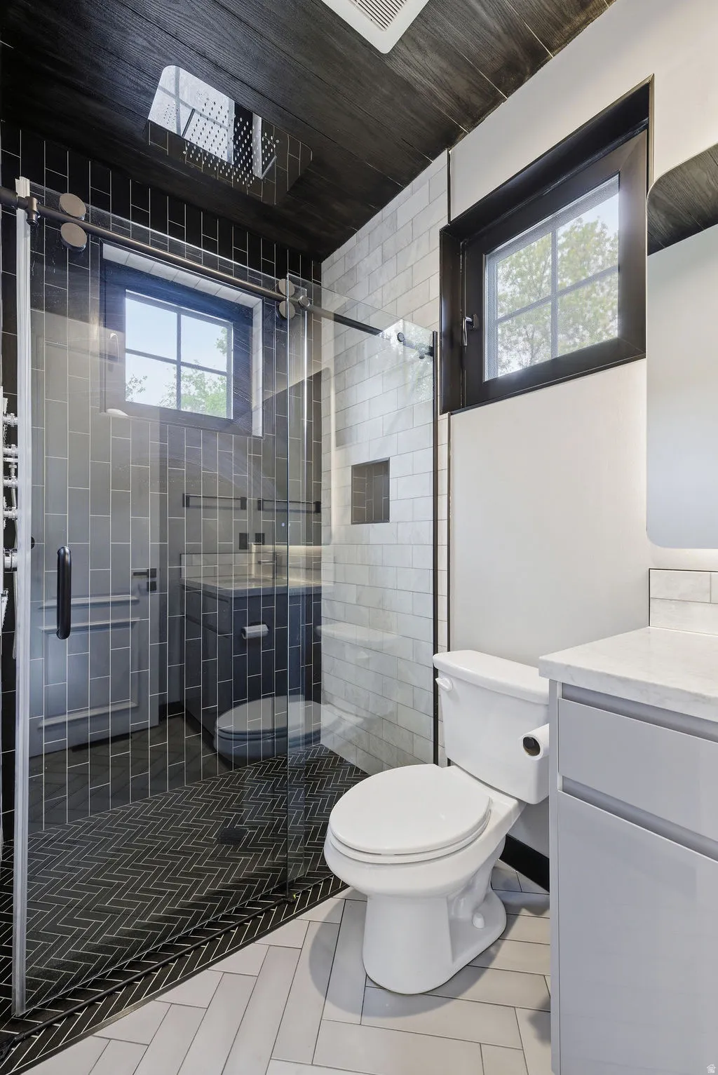 Contemporary bathroom featuring a glass-enclosed shower with a rainfall showerhead, dark wood-finish ceiling, and light gray herringbone tile flooring
