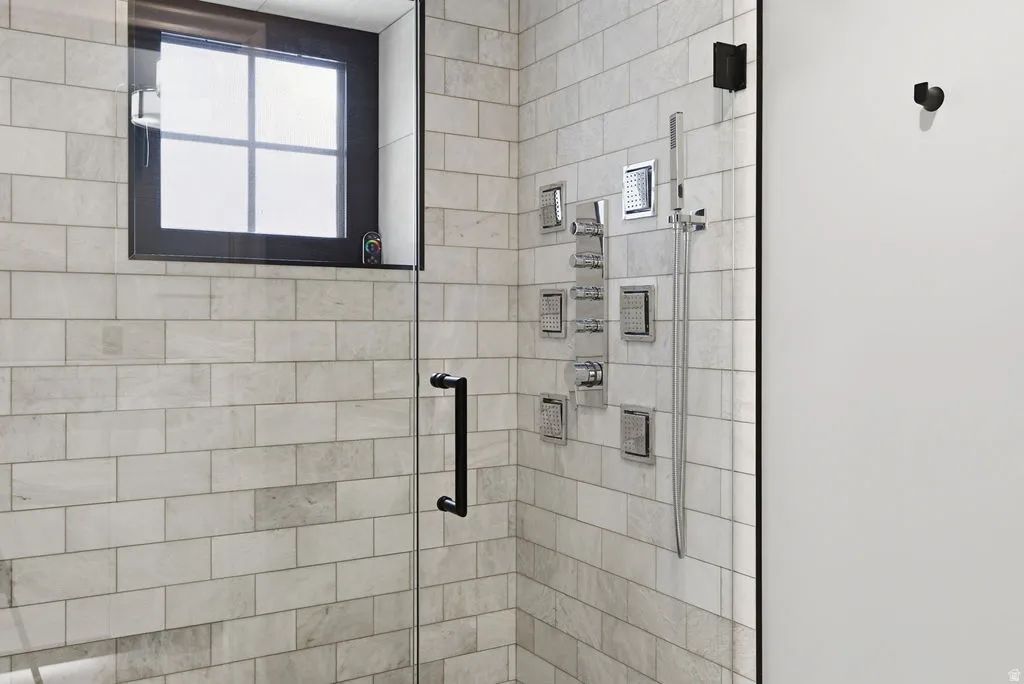 Glass-enclosed shower featuring subway-style tiling, a multi-setting shower system, and a black-framed window