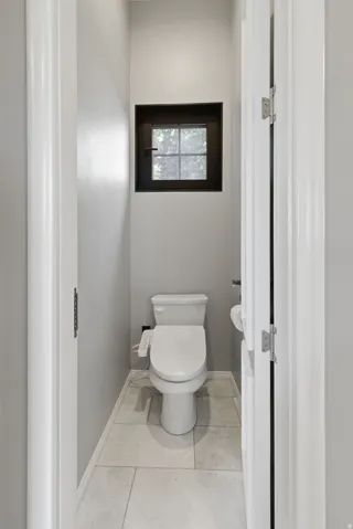 Powder room featuring a square window with dark trim, light-toned tile flooring, and a white toilet