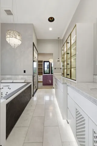 Elongated bath area featuring a built-in jetted tub with dark-toned paneling, a large mirror, and a contemporary chandelier