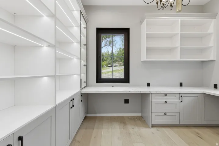 Built-in custom cabinetry with integrated lighting, a spacious L-shaped desk with a light-toned countertop, and wood-finish flooring