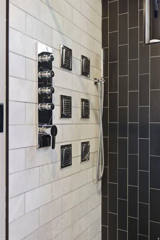 Shower featuring an integrated control panel with multiple body sprays, a handheld shower fixture, and contrasting subway tile in black and white finishes