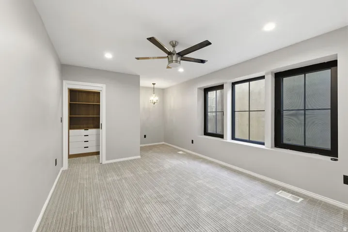 Room featuring three black-framed windows, a ceiling fan with light fixture, recessed lighting, and patterned carpeting