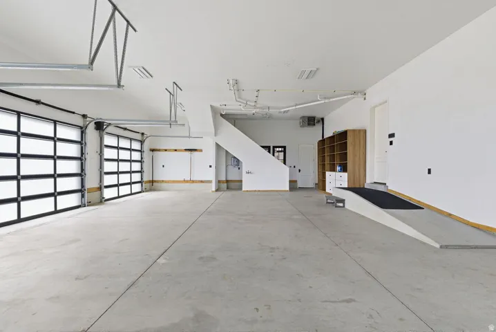 Spacious garage featuring a concrete floor, two modern glass-paneled garage doors, white painted walls, and an interior ramp