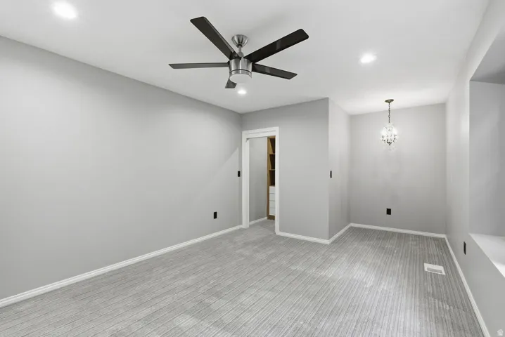 Spacious room featuring light gray carpeting and walls, a modern ceiling fan, recessed lighting, and a crystal chandelier