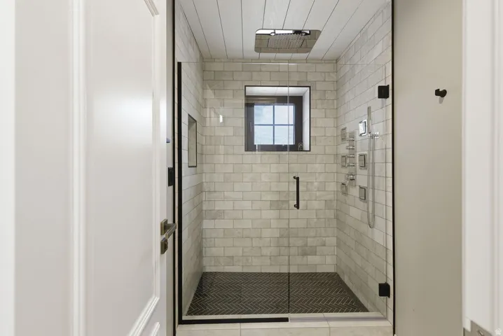 Glass-enclosed shower with subway tile walls and dark herringbone-patterned floor